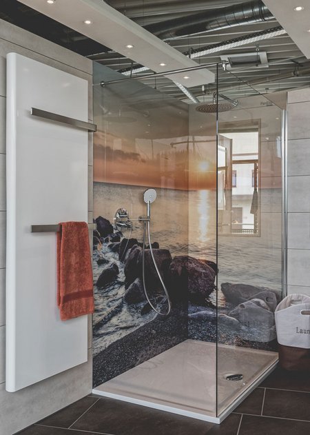 Moderne Dusche mit großem Glasabtrennsystem, Fotowand mit Sonnenuntergang am Meer, Regendusche und weißem Badheizkörper.